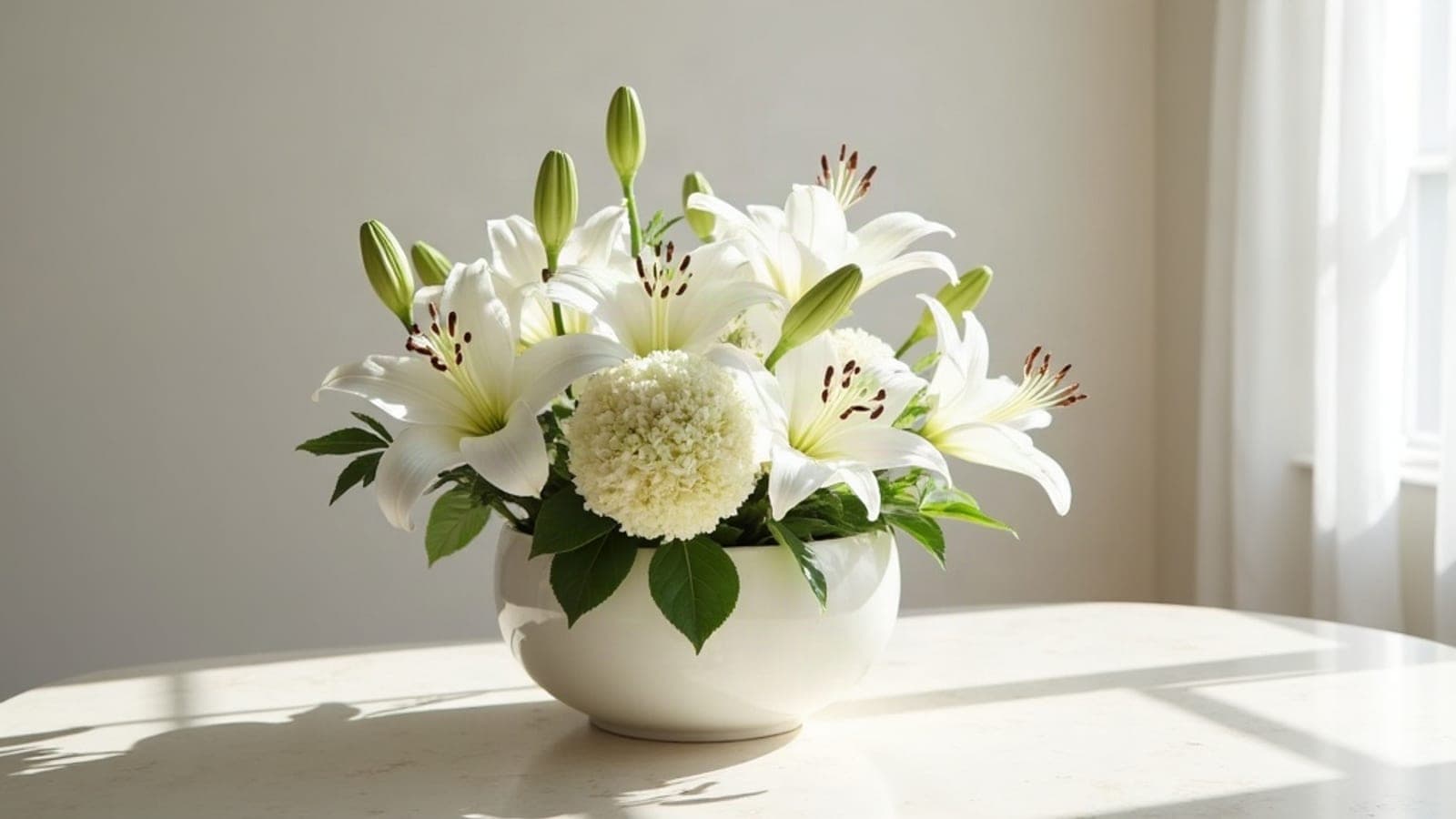 Une vasque de lys blancs et d'hortensias posée sur une table claire, près d'une fenêtre