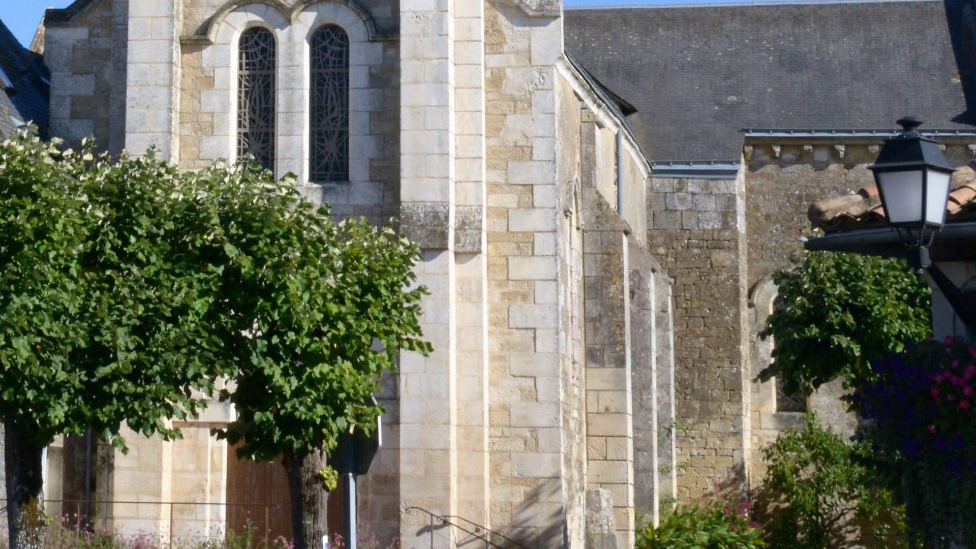L'église Saint-Hilaire de Rouillé, murs de pierre claire et vitraux derrière les tilleuls du bourg